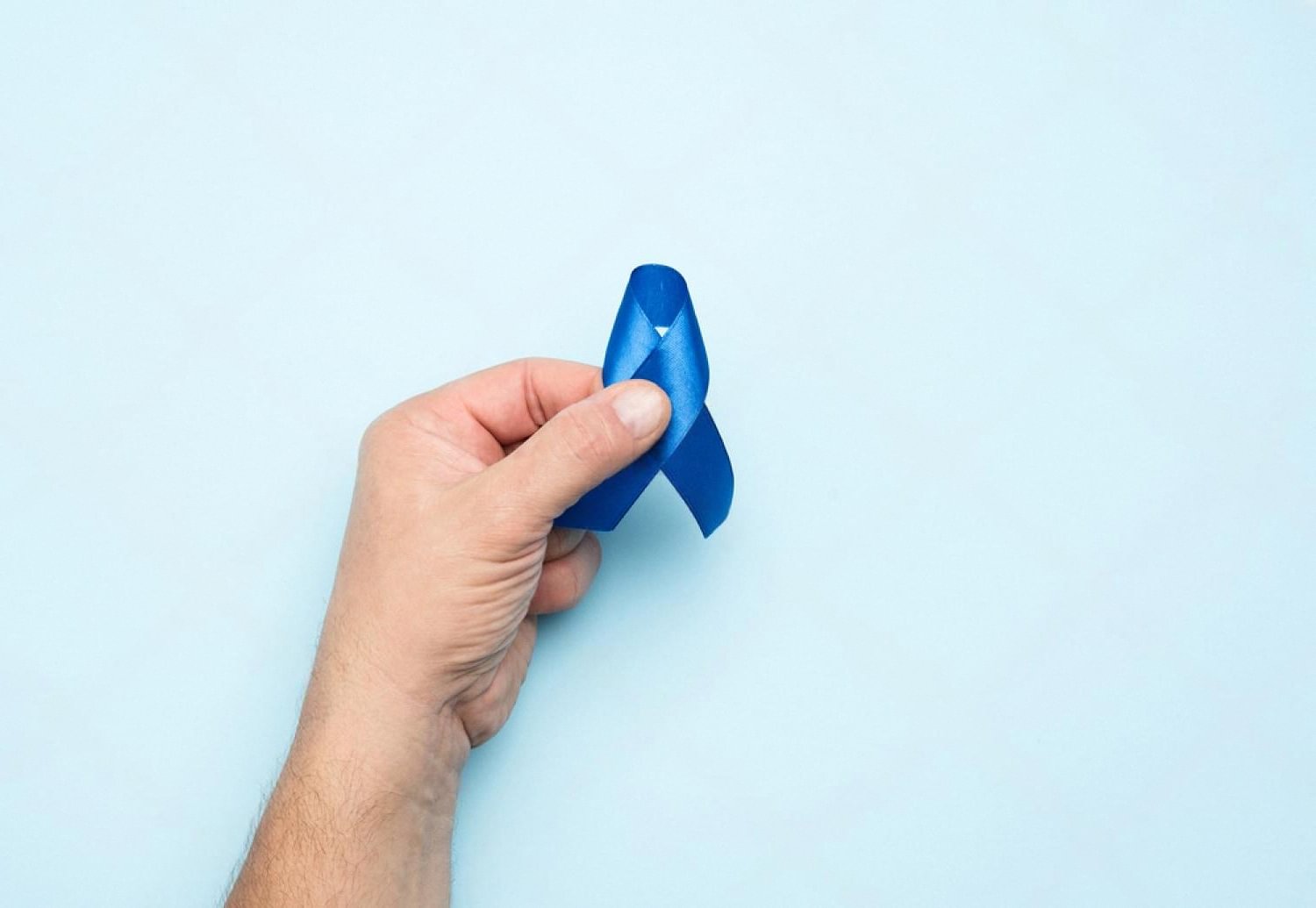 Hand holding a blue ribbon symbolising colorectal cancer awareness